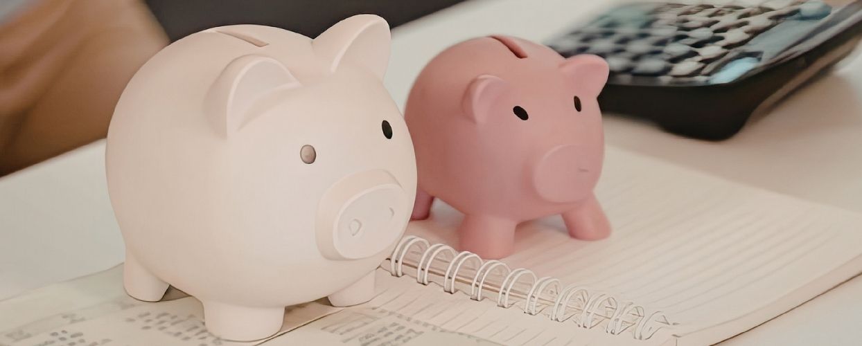 Zwei Sparschweine auf einem Rechenblock.